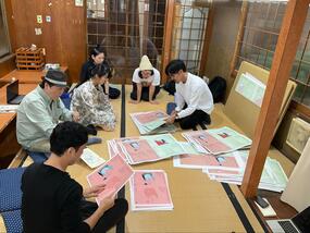 畳の部屋で光島氏をはじめ6名が座り、大判の印刷物を囲みながら確認をしている様子の写真