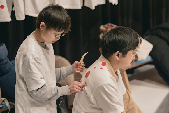 過去に実施したTシャツワークショップの様子。親子で参加しているペア、男の子がTシャツを着たお父さんの背中に赤いドットのシールを貼っている。